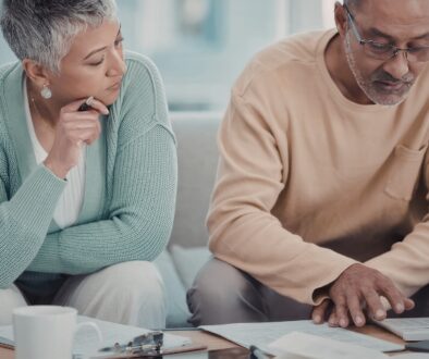 A couple sitting at their coffee table looking at financial documents and using a calculator.