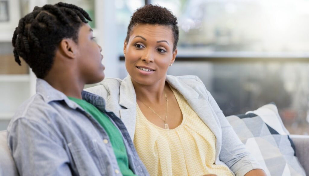 A mother talking with her teenage son on the couch.
