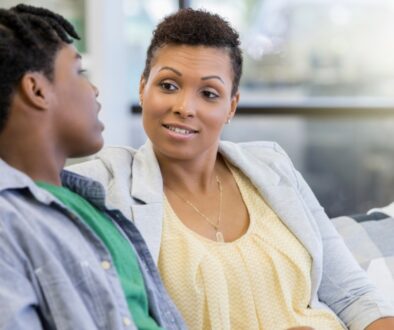 A mother talking with her teenage son on the couch.