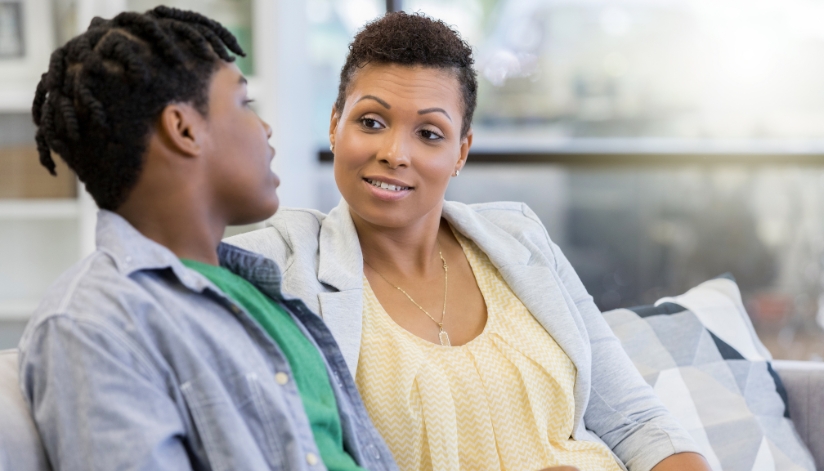A mother talking with her teenage son on the couch.