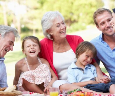 Grandparents, parents, and young children smiling and laughing while enjoying a summer picnic.