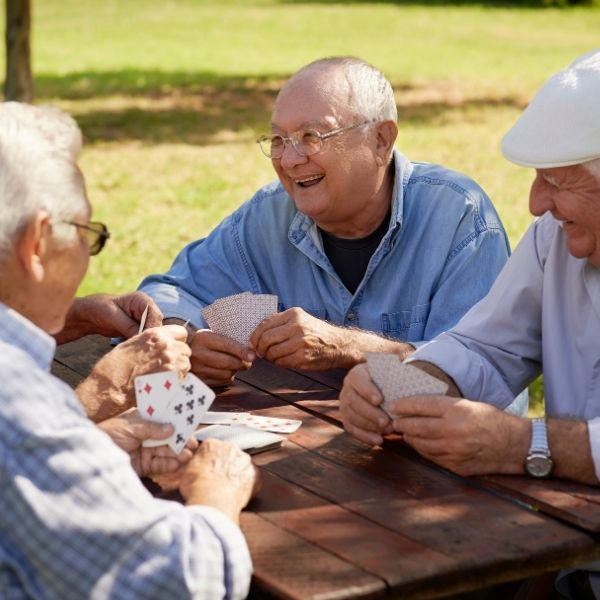 Four older men play cards and smile outdoors in Wisconsin, discussing fiduciary financial advisors and planning their future.
