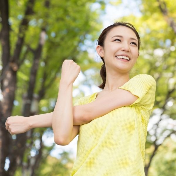 A woman in a yellow shirt smiles and stretches her arm outdoors among green trees in Wisconsin, where fiduciary advisors serve.