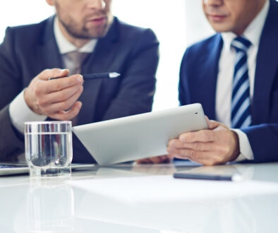 Men in suits sitting in a conference room looking at a tablet.