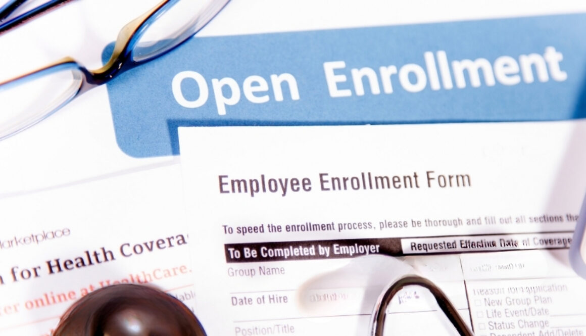 Open enrollment paperwork and employee enrollment form with eyeglasses and a pen.