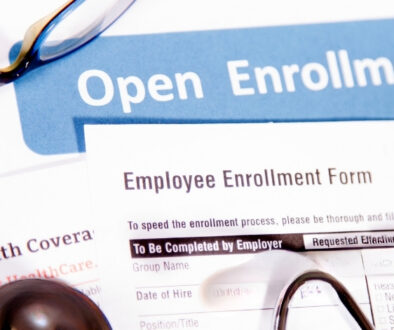 Open enrollment paperwork and employee enrollment form with eyeglasses and a pen.