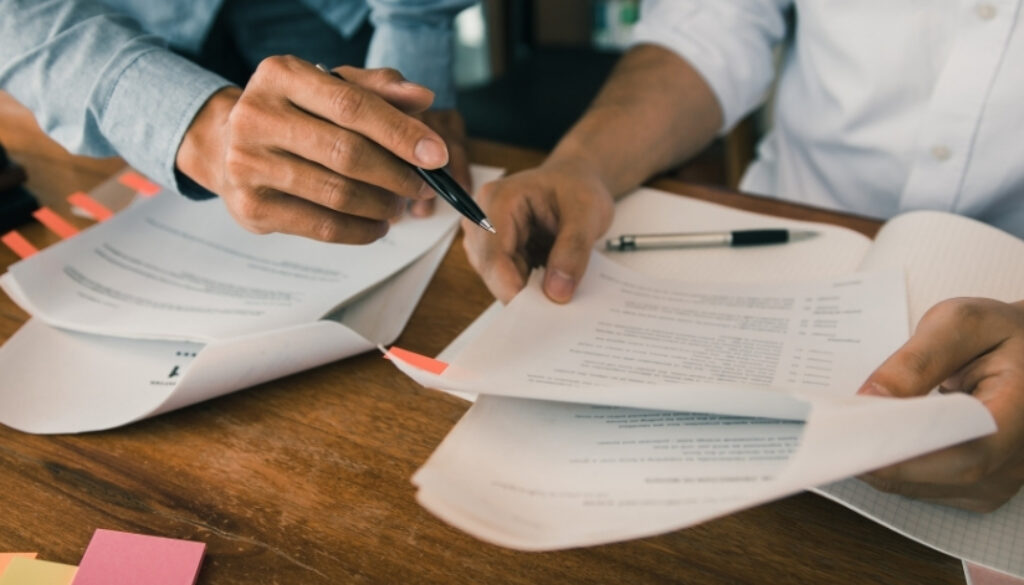 People dressed in business casual clothing holding pens and reviewing paperwork.
