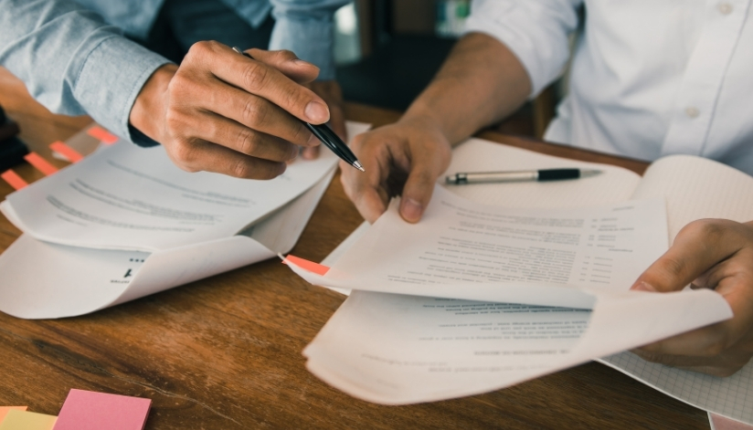 People dressed in business casual clothing holding pens and reviewing paperwork.