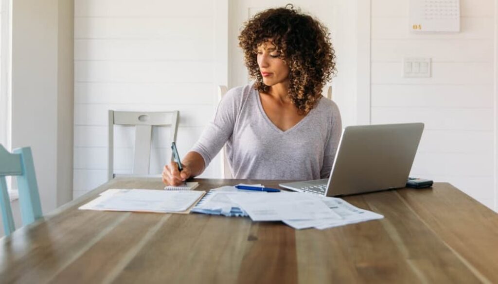 Woman reviewing financial paperwork at a table with a laptop.