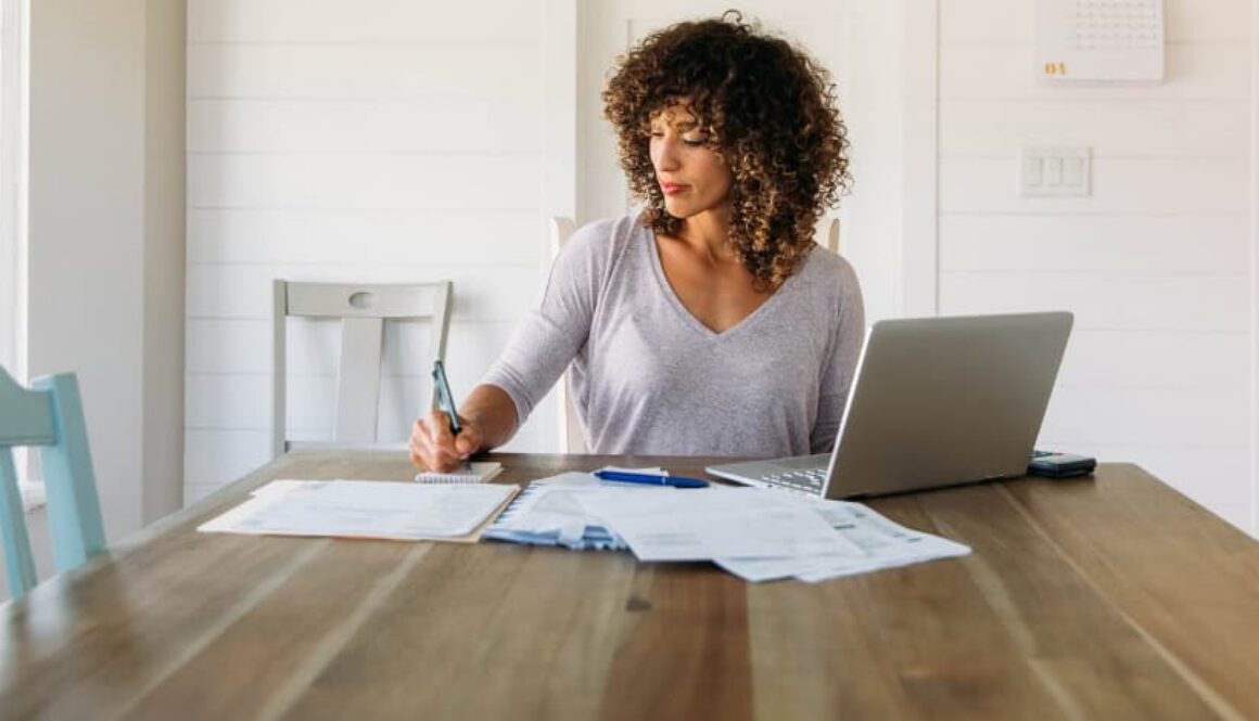 Woman reviewing financial paperwork at a table with a laptop.