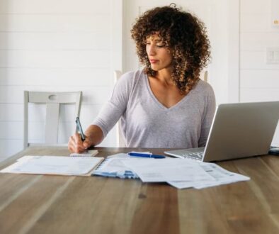 Woman reviewing financial paperwork at a table with a laptop.