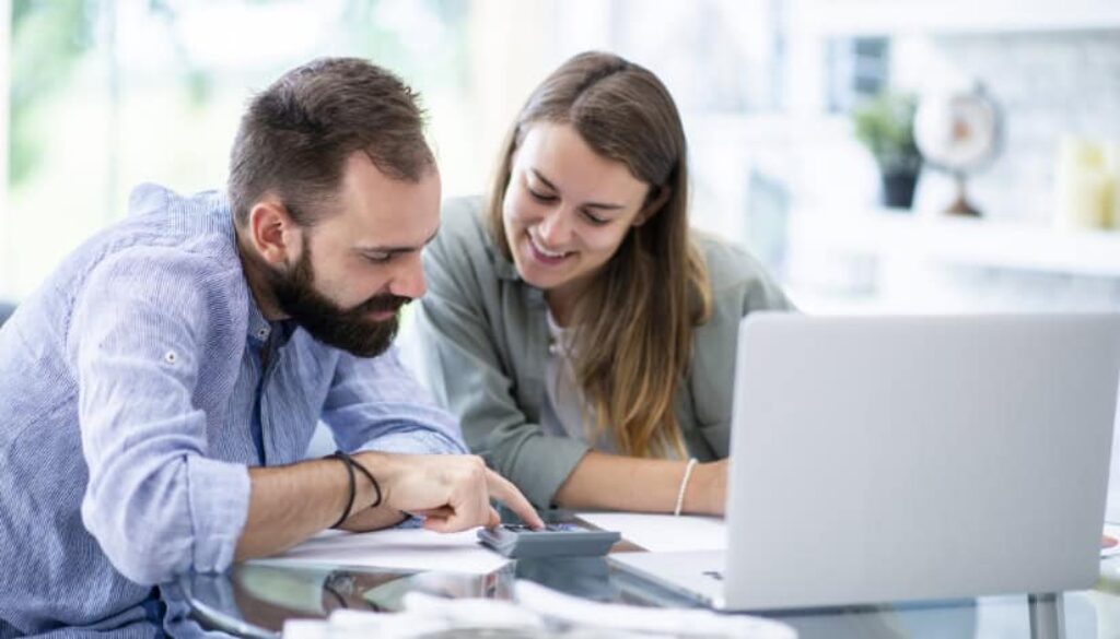 Couple reviewing finances together with a calculator and laptop.