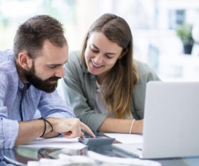 Couple reviewing finances together with a calculator and laptop.