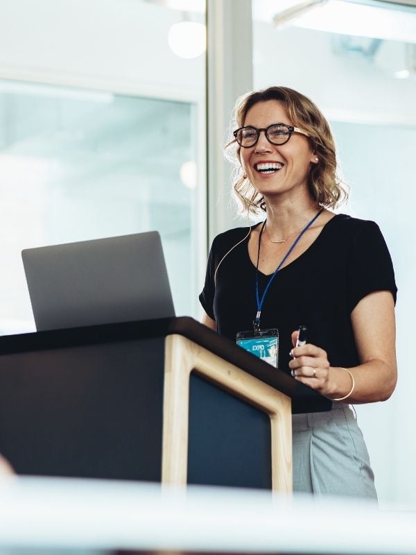 A smiling woman in glasses presents tax planning strategies at a podium with a laptop for Advisors Management Group in Wisconsin.