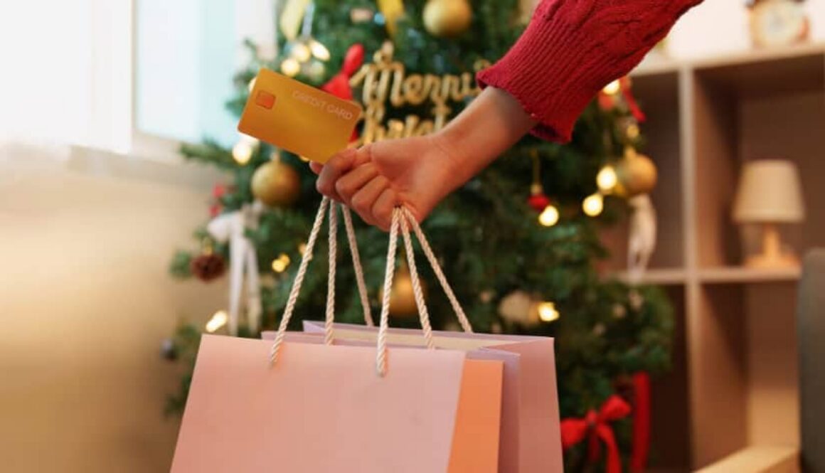 Person holding shopping bags and a credit card in front of a Christmas tree.