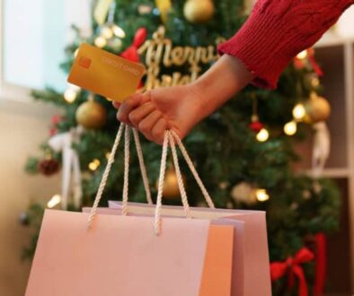 Person holding shopping bags and a credit card in front of a Christmas tree.